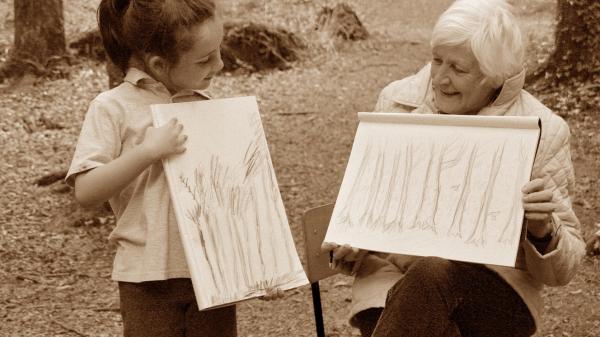 An elderly lady and a female child comparing drawings of trees.