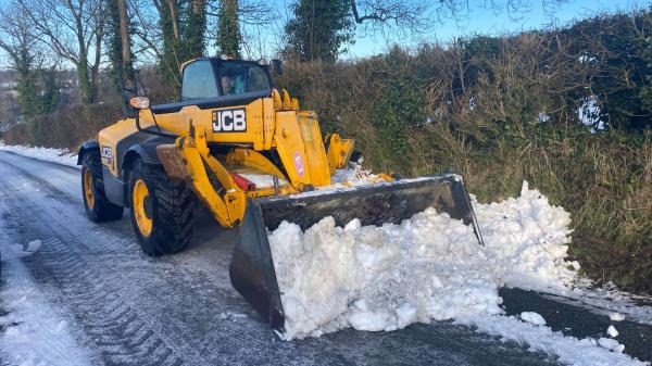 A yellow JCB front loader clearing snow from a rural road.