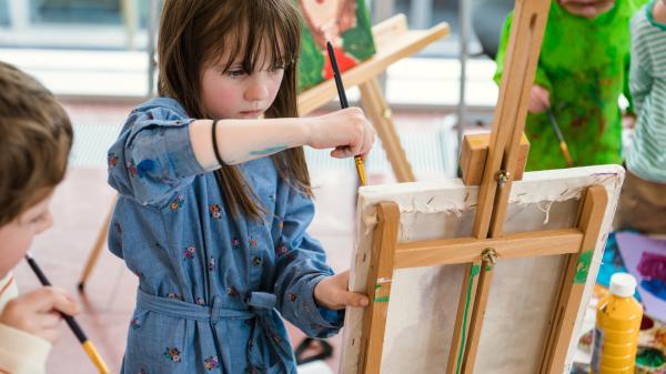 Young girl painting as other children watch.