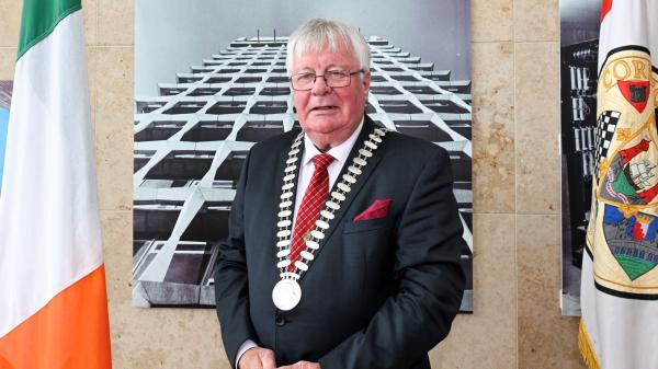 A man standing in front of two flags wearing a mayoral chain in a suit