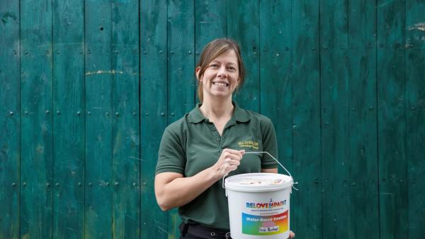 Person holding a paint bucket in front of a teal wooden fence.