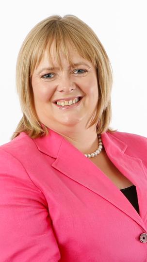 Woman in a pink blazer with a pearl necklace against a white background.