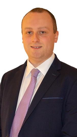 Man in a navy-blue suit with a pink tie against a white background.