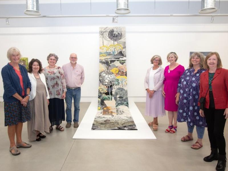 Group of people standing next to a tapestry at Timelines art exhibition