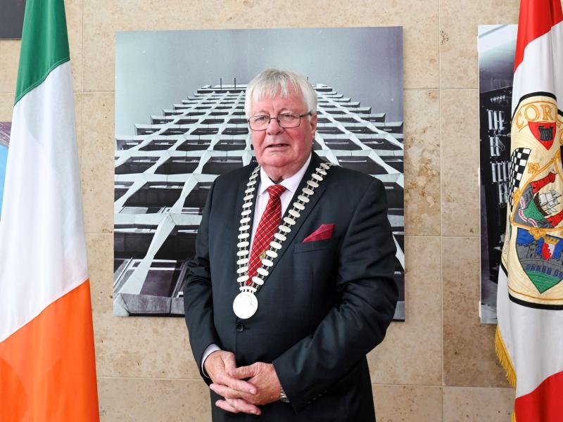 A man standing in front of two flags wearing a mayoral chain in a suit