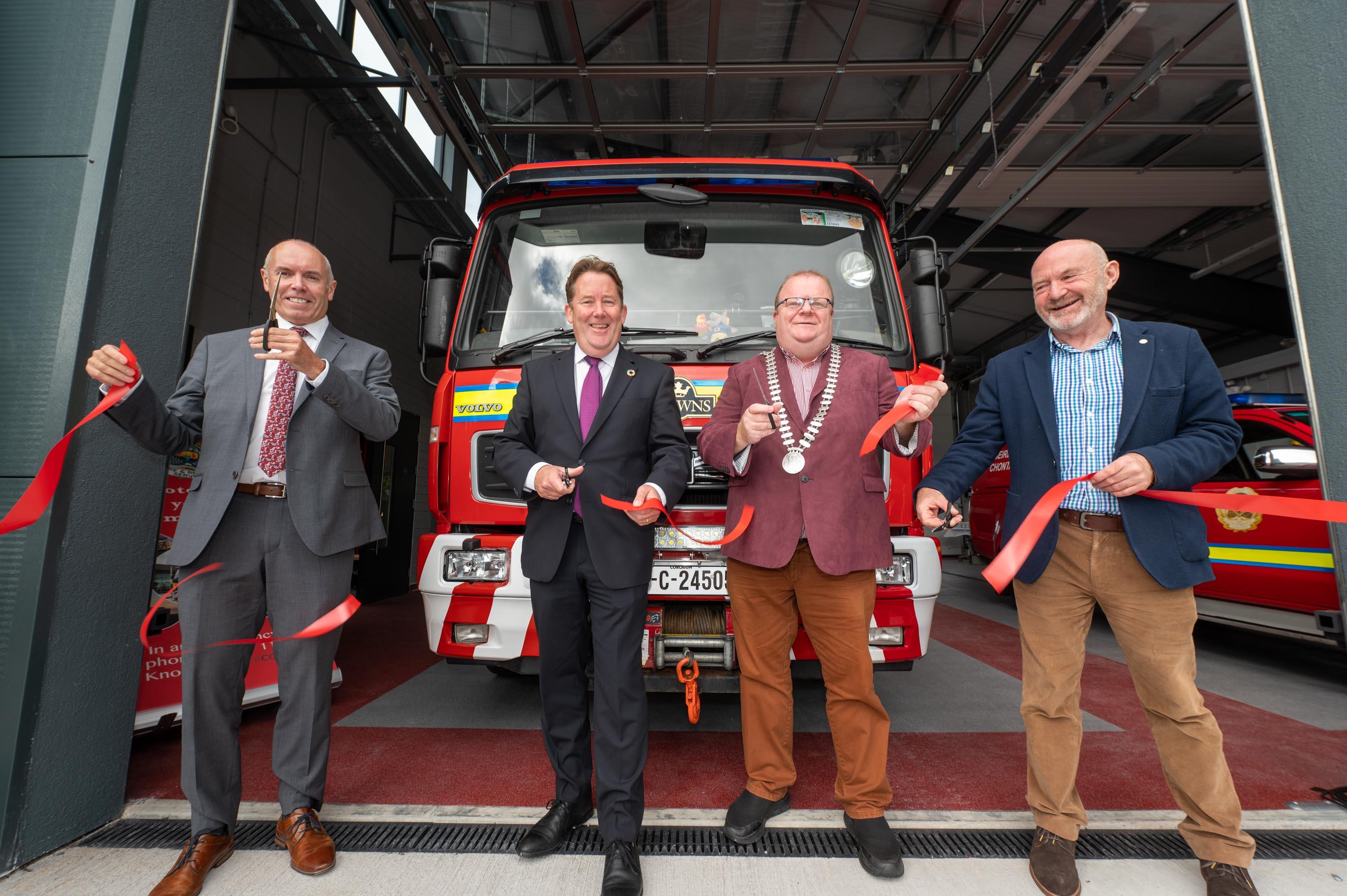 The Mayor of the County of Cork with a group of 3 men cutting a red ribbon infront of a Firetruck
