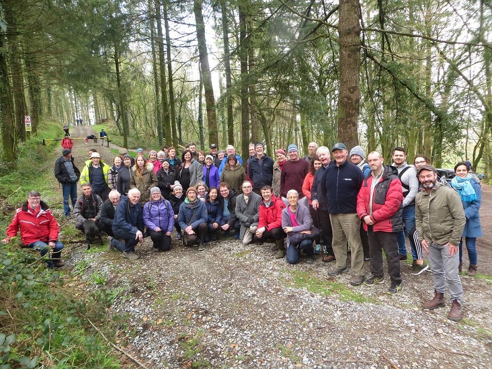 A group of approximately 30 people in a forrest surrounded by trees.