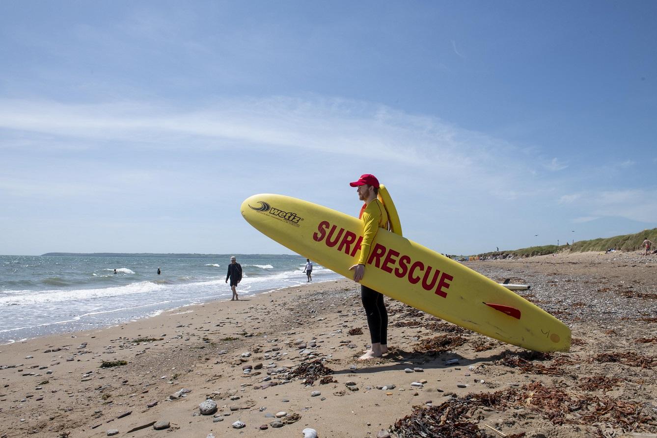 A Cork County Council beach lifeguard holding a surf rescue board looking out towards the sea.