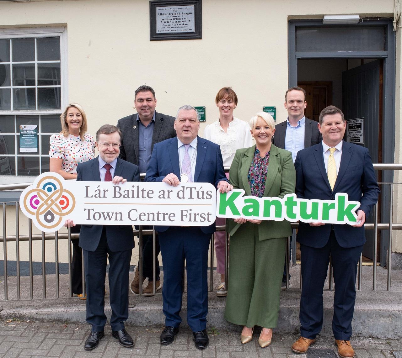 Elected members and staff of Cork County Council holding 2 signs, one saying "Town Centre First" and the other saying "Kanturk2.