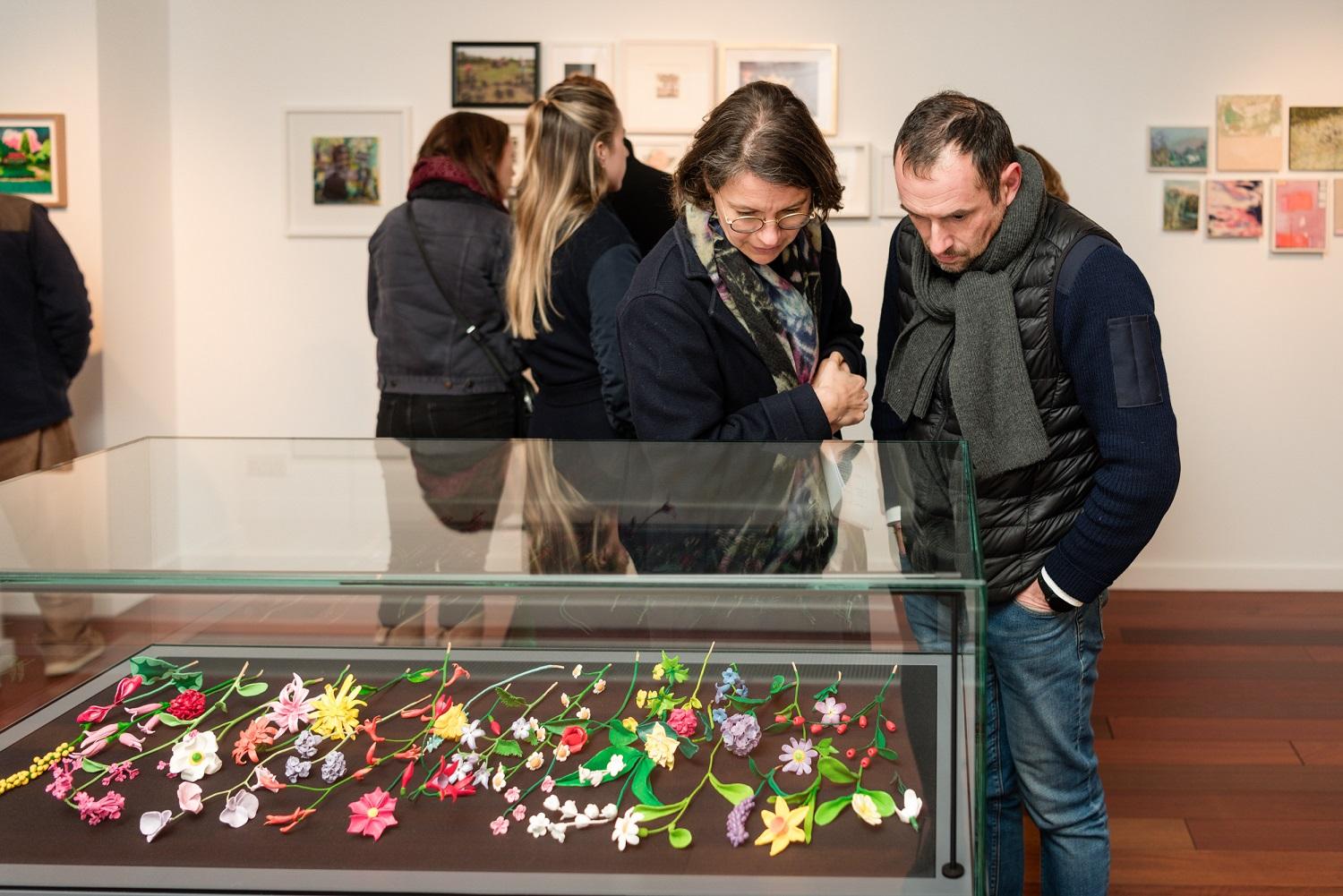 A mand and woman looking at an exhibit of flowers in a glass case.