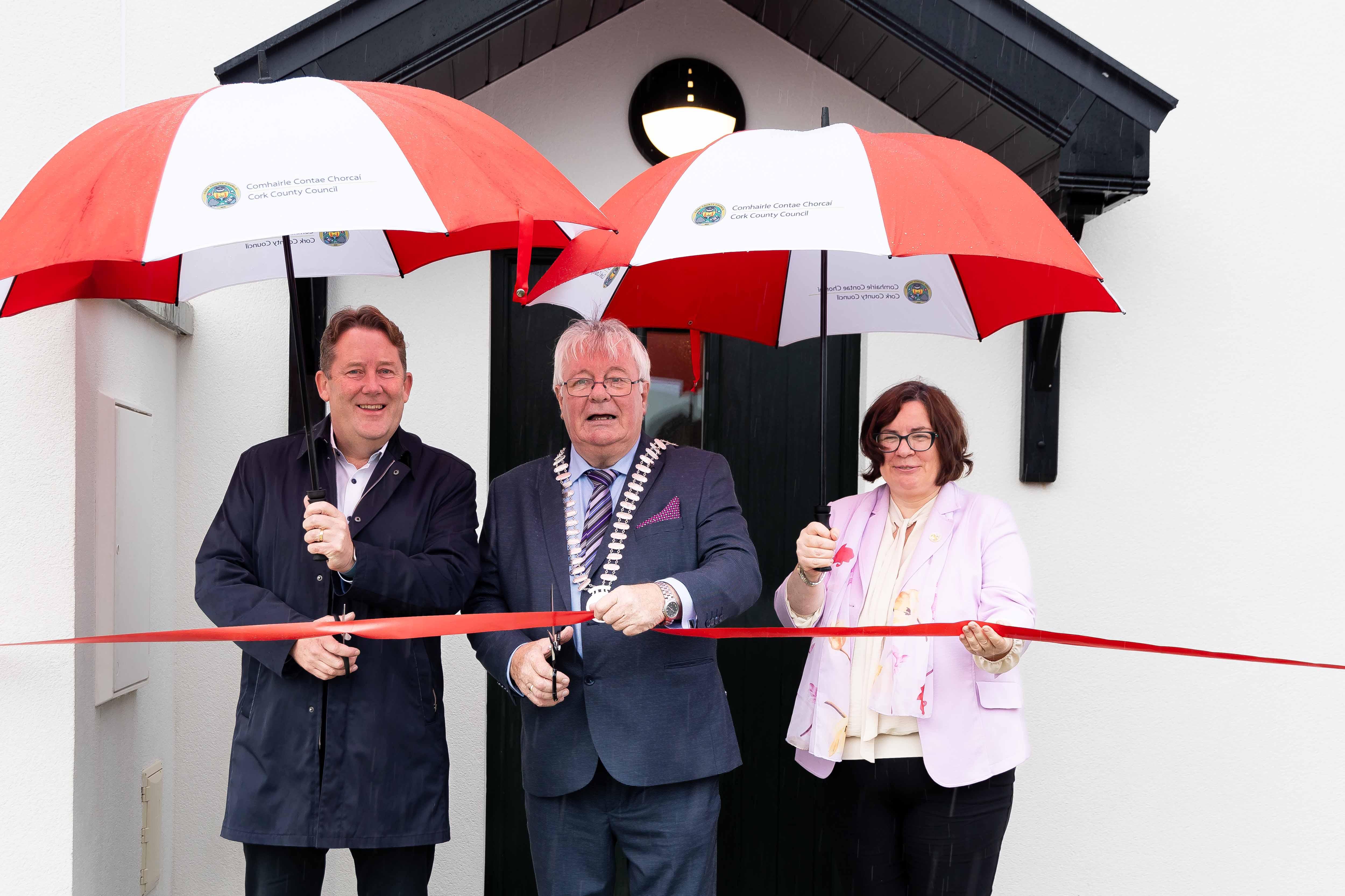 3 people holding umbrellas and cutting a ribbon