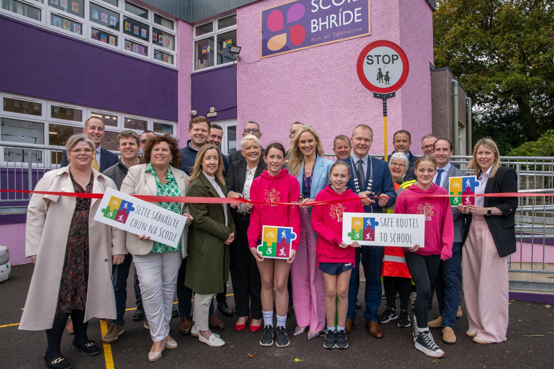 A group of people in front of a school cutting a red ribbon