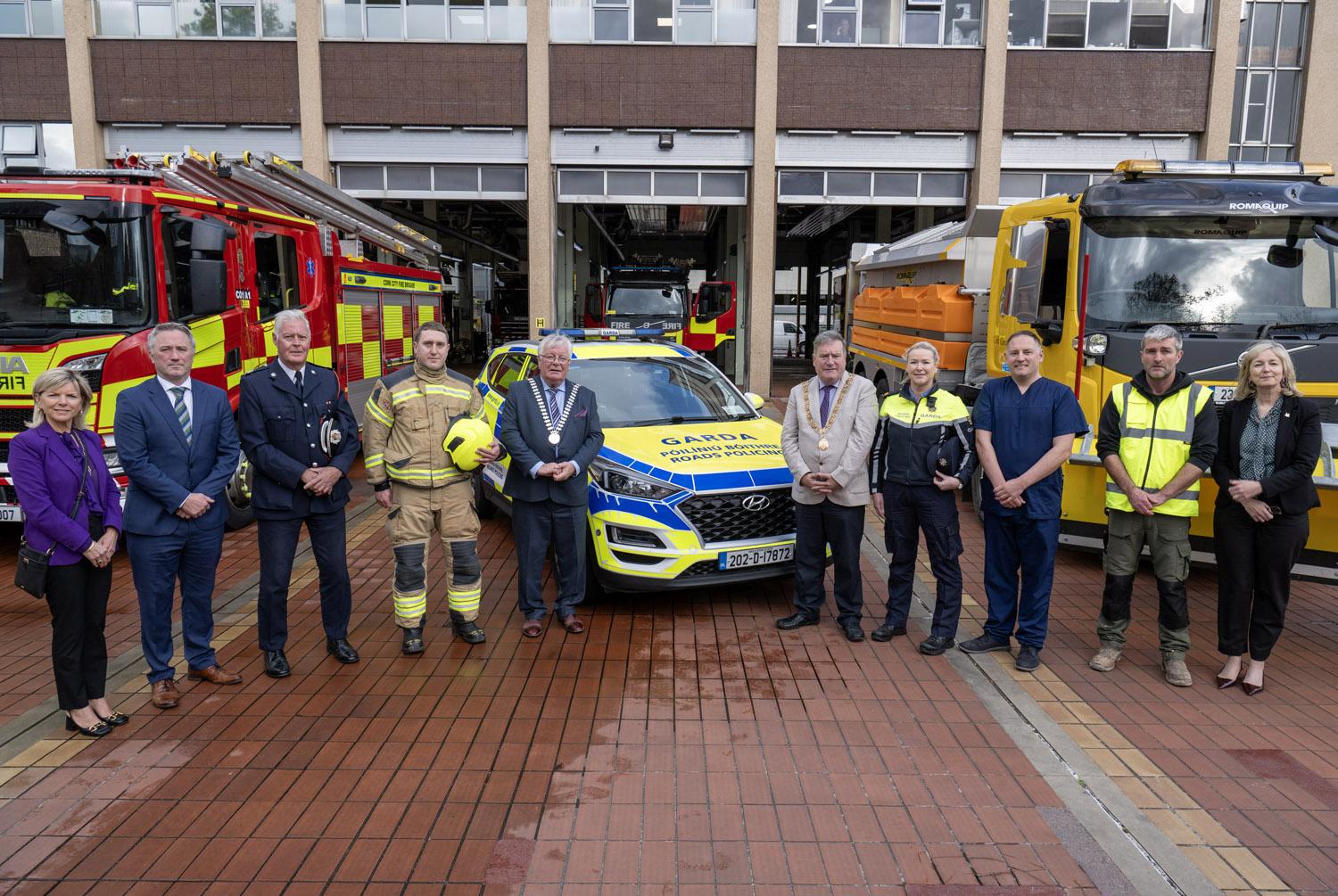 A group of people in suits and high visibillty vests stading in front of a fire engine and a garada car