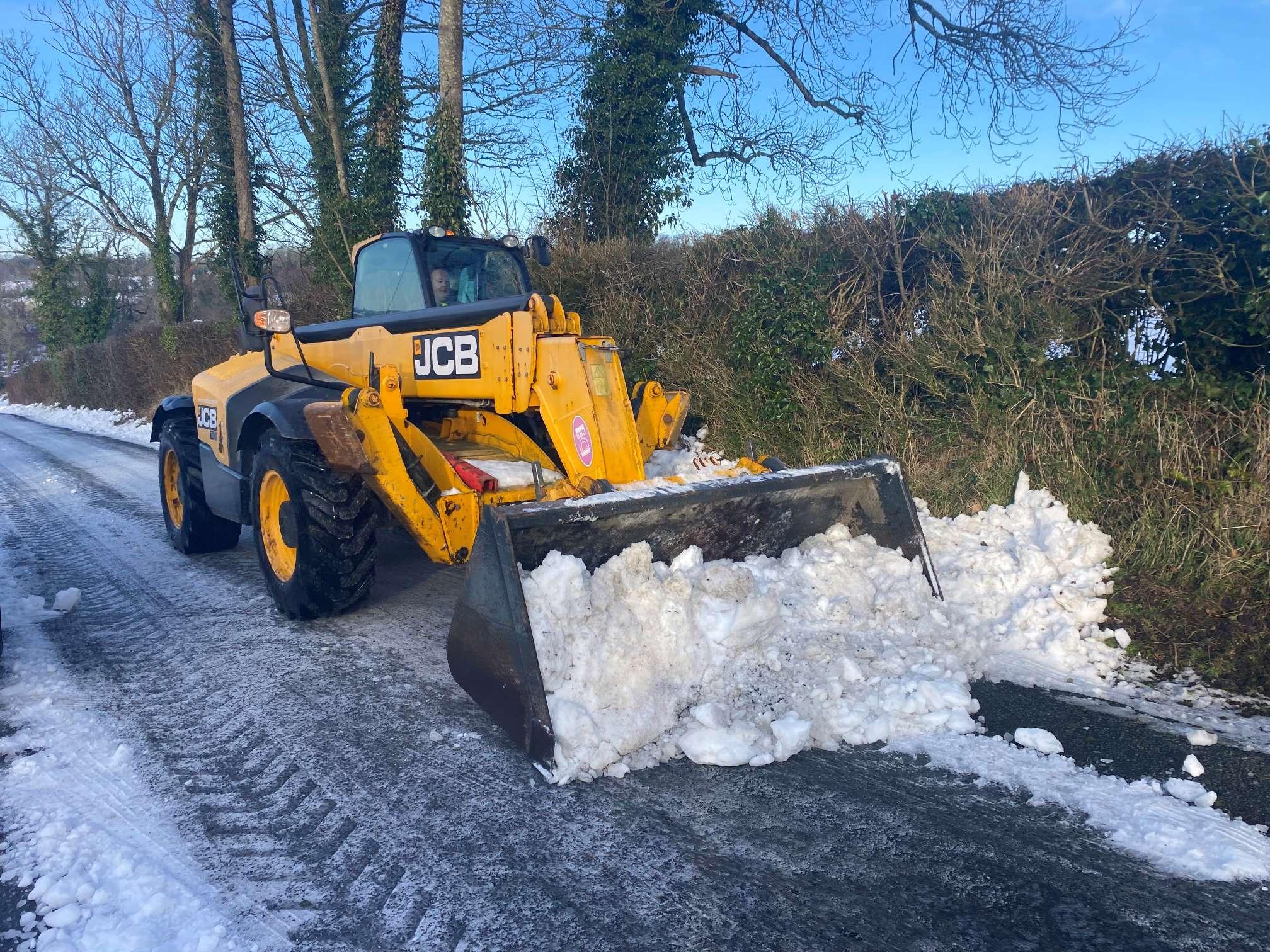 A yellow JCB front loader clearing snow from a rural road.