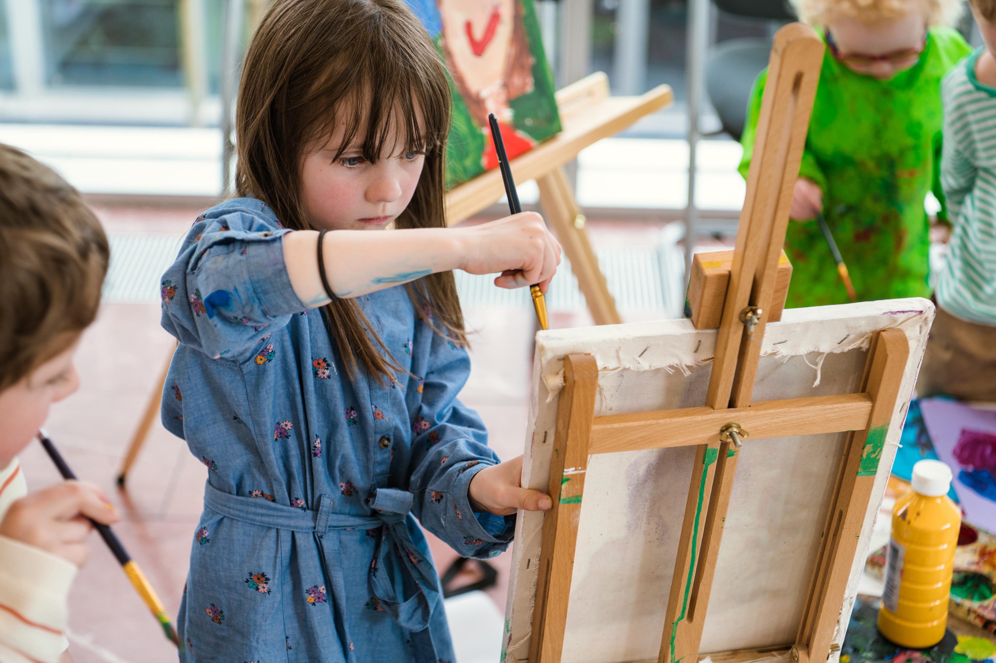 Young girl painting as other children watch.