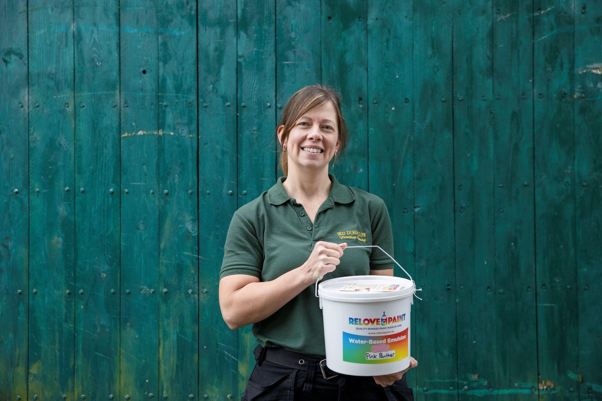 Person holding a paint bucket in front of a teal wooden fence.