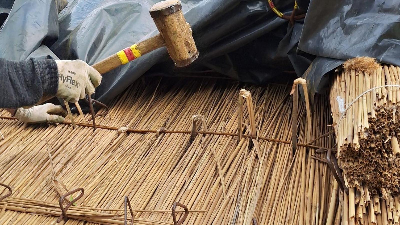 A hand hammering a thatched  roof