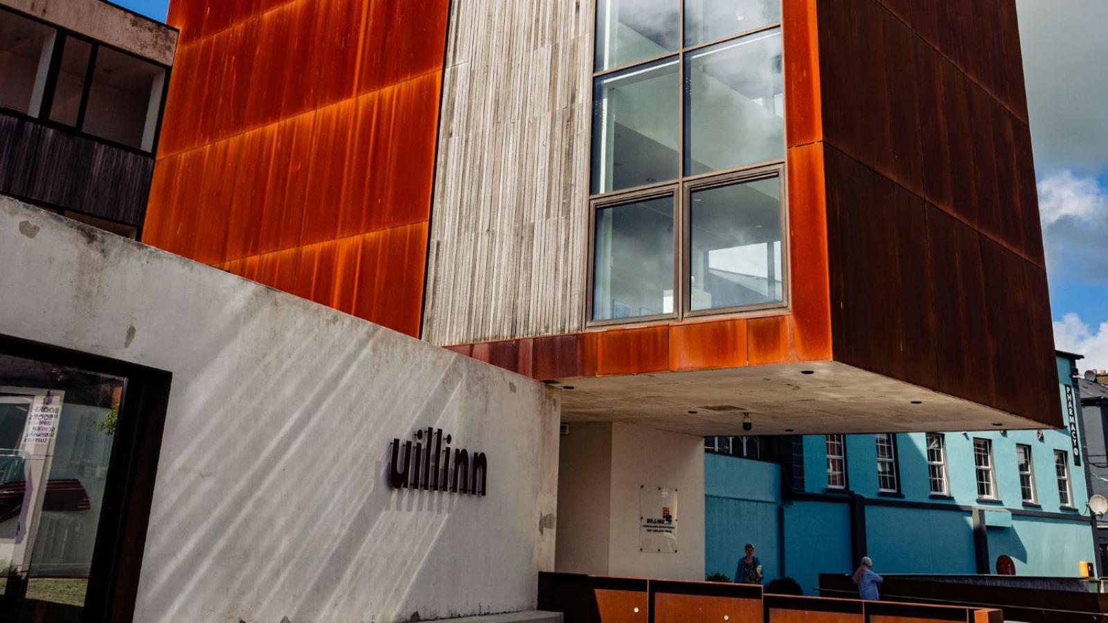 Modern building with rust-colored facade and large window, labeled "Uillinn."